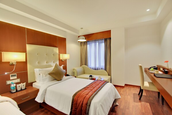 Une chambre d’hôtel avec un grand lit, un bureau, une chaise, un canapé et une fenêtre avec des rideaux.