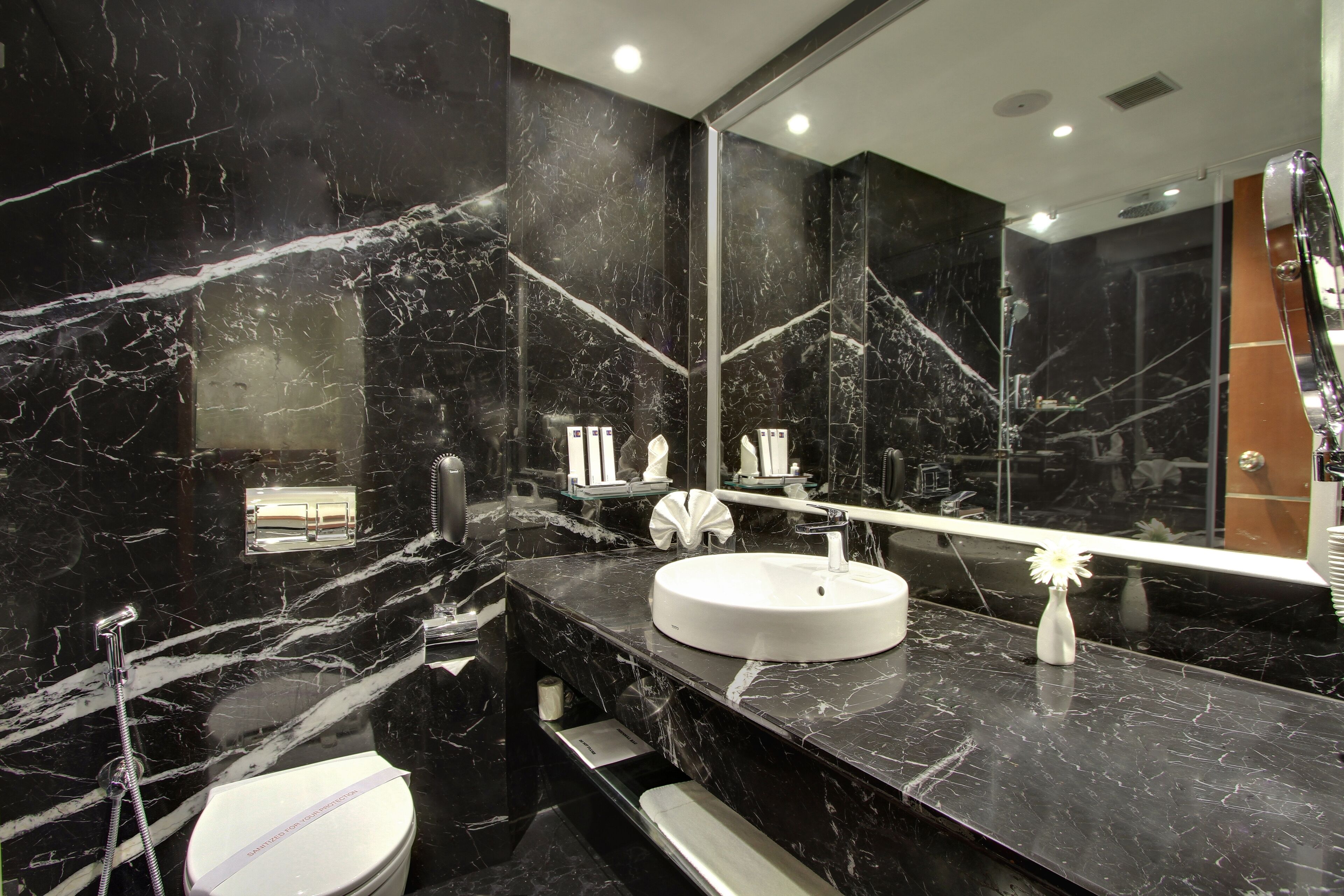 A modern bathroom with a black marble sink, a large mirror, and a toilet.