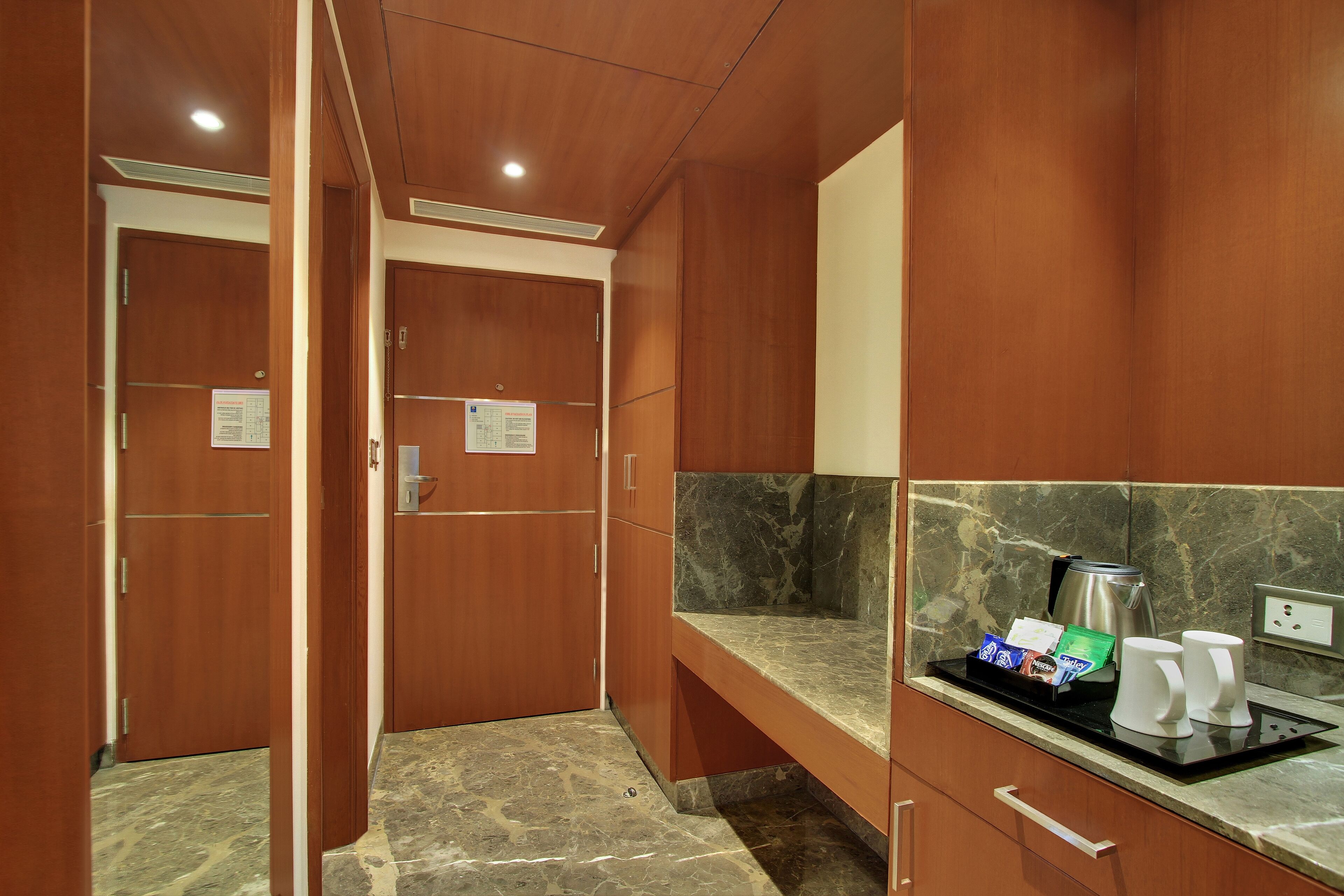 A hotel room with wooden cabinets, a marble countertop, a coffee maker, and a tray with coffee cups and snacks.