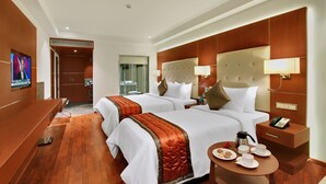 A hotel room with two beds, a TV, a coffee table with breakfast items, and a bathroom visible through an open door. - Lavender Premier (Bengaluru)
