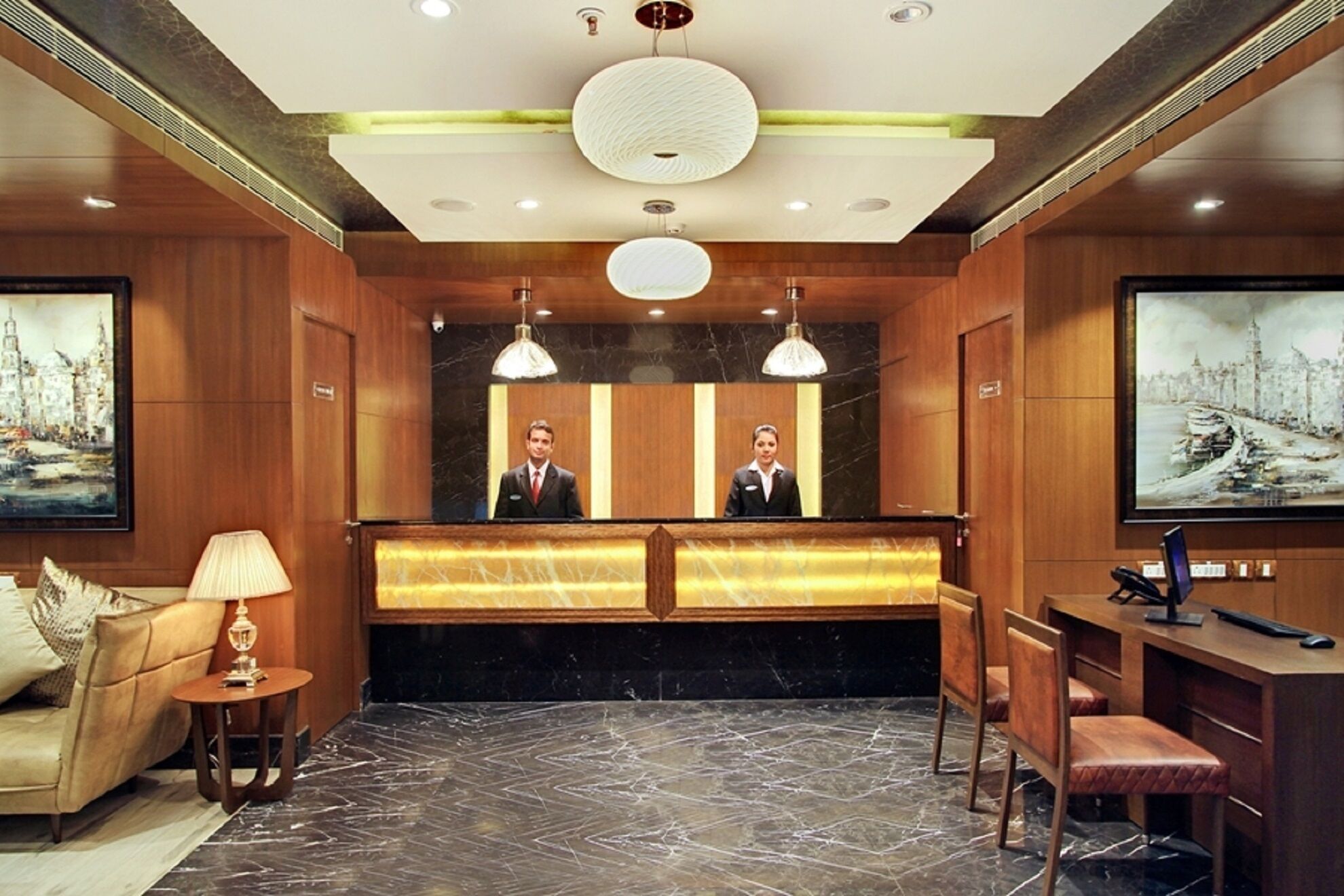 A hotel reception area with a marble floor, wooden paneling, a reception desk, a sofa, and a painting on the wall.