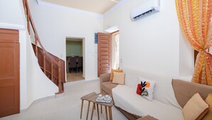 Una sala de estar con una escalera, un sofá, una mesa de centro y un equipo de aire acondicionado.