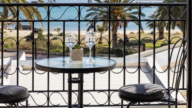 A balcony with a table and two chairs, overlooking a beach and mountains.