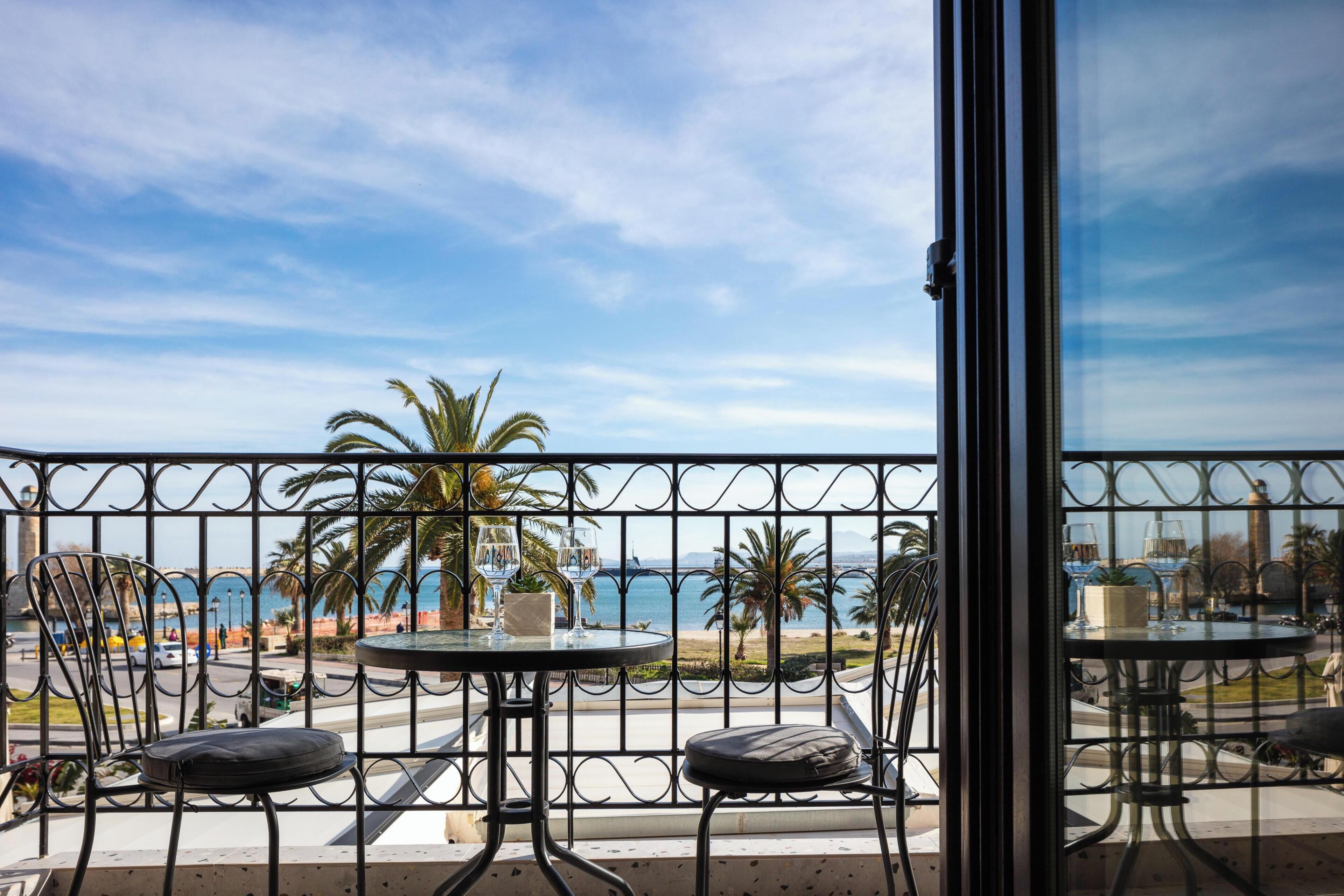 A balcony with two tables and chairs, overlooking a beach and the sea.