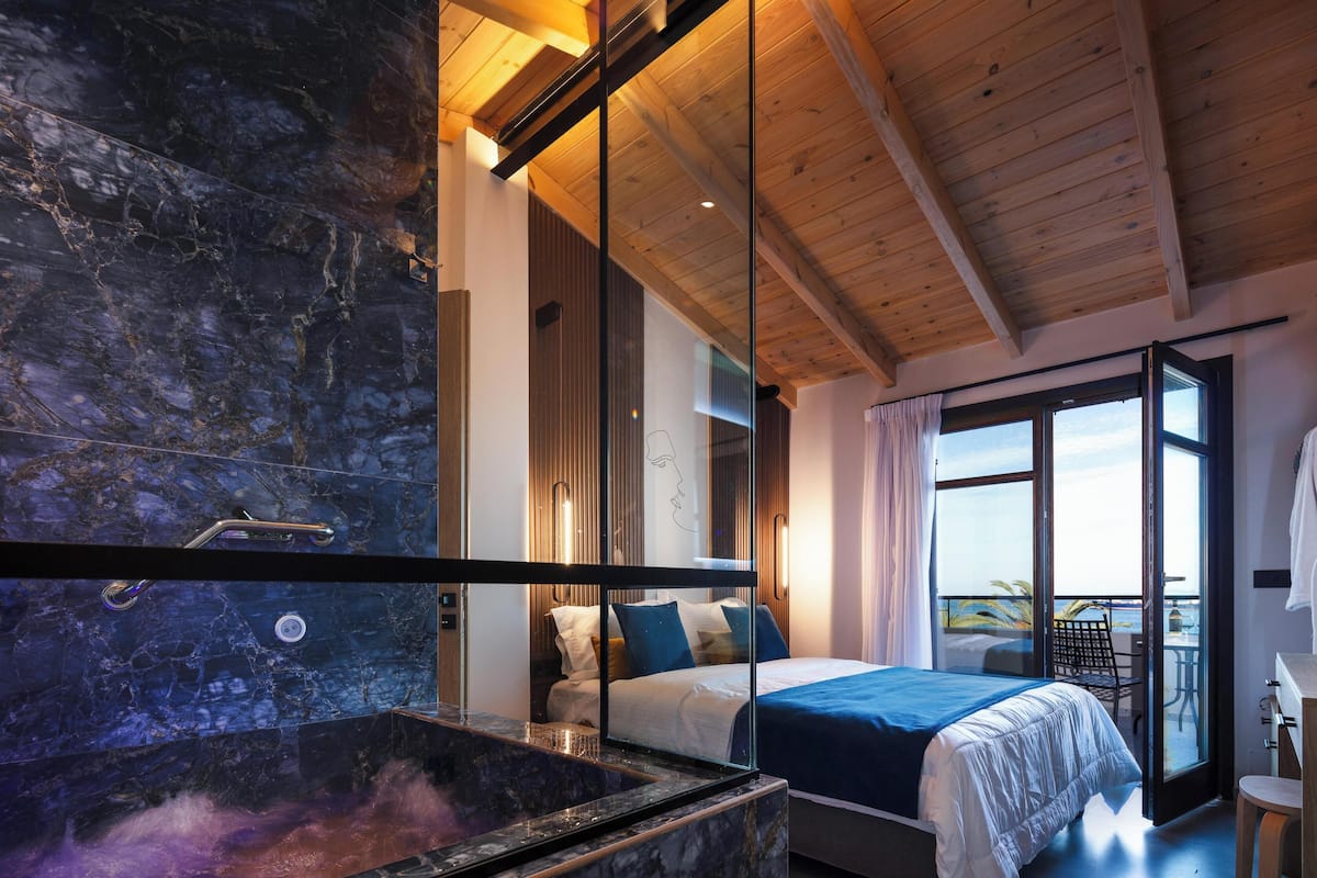 A modern bedroom with a large bed, a glass shower enclosure, and a balcony with a view.