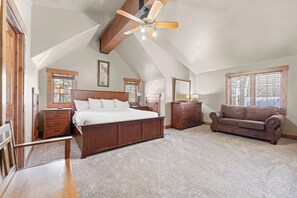 Een slaapkamer met een groot bed, houten meubels, een plafondventilator en ramen met zonwering.