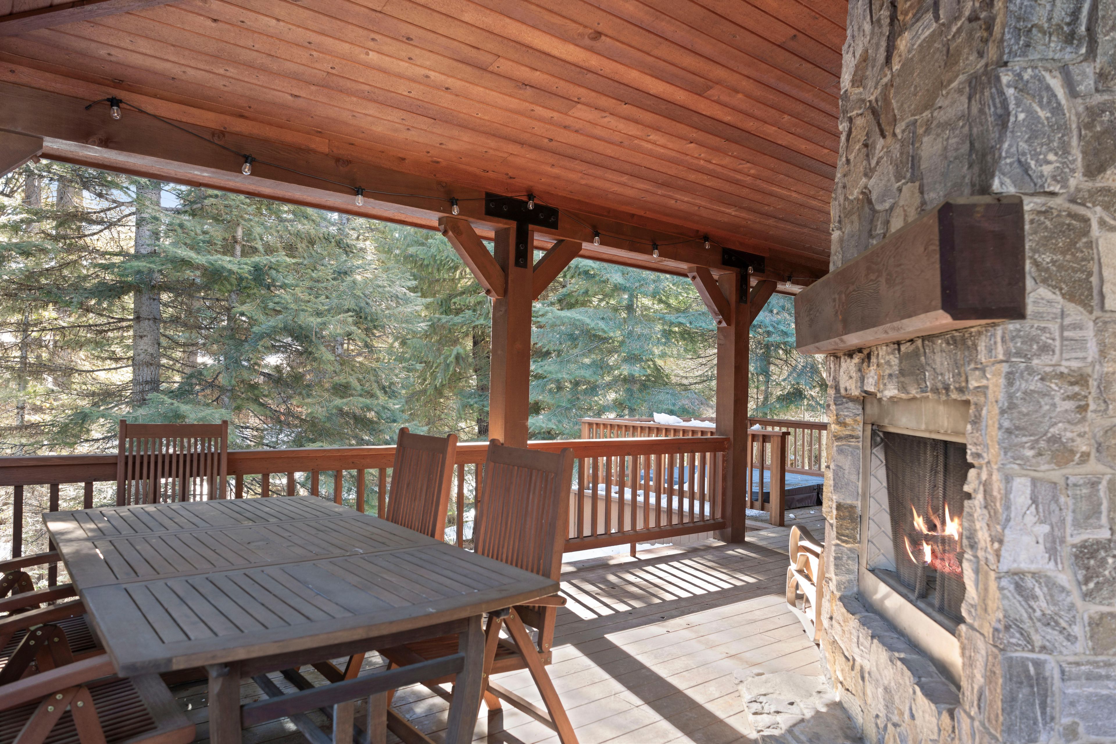 A covered outdoor area with a stone fireplace, wooden deck, and seating.