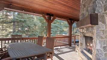 A covered outdoor area with a stone fireplace, wooden deck, and seating.