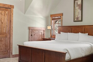 Un dormitorio con cama de madera, una mesita de noche, un armario de madera y una ventana con vistas a árboles.