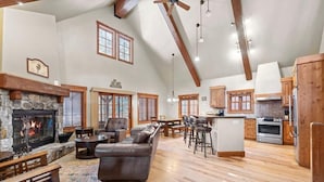 A spacious living room with a fireplace, a leather sofa, wooden flooring, and a kitchen area with wooden cabinets and appliances.