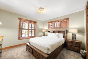 A bedroom with a wooden bed, two bedside tables with lamps, a window with shutters, and a ceiling light fixture. - Discovery Retreat | Exclusive Tamarack Perks (Donnelly)