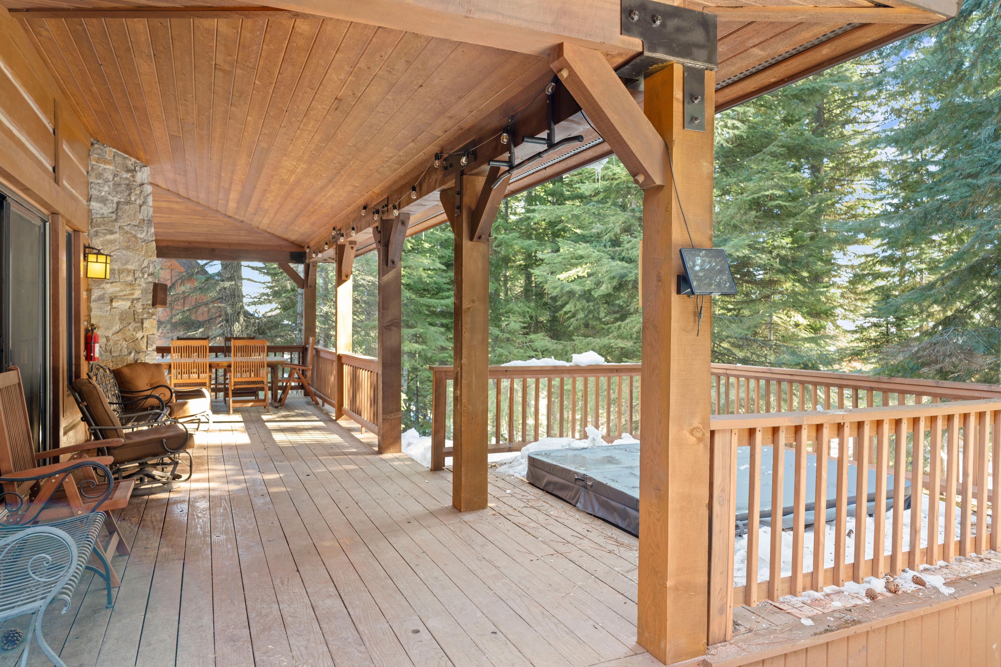 A wooden deck with a covered seating area, stone wall, and a view of a forest.
