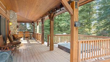 A wooden deck with a covered seating area, stone wall, and a view of a forest.