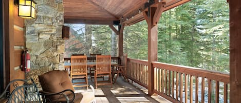 Una terraza de madera con muros de piedra, mobiliario exterior y vistas a árboles.