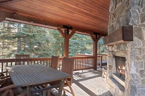 A covered outdoor area with a stone fireplace, wooden deck, and seating. - Discovery Retreat | Exclusive Tamarack Perks (Donnelly)