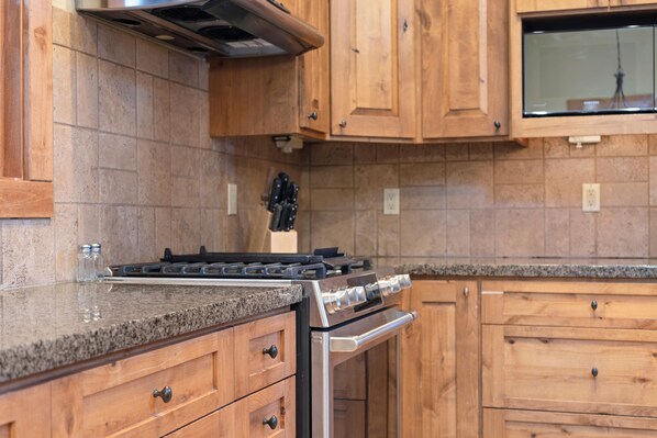 Una cocina con gabinetes de madera, estufa de acero inoxidable y encimeras de granito.