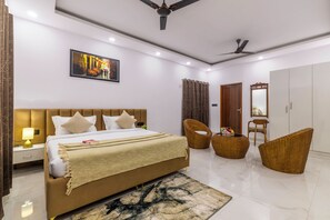 A modern bedroom with a large bed, two wicker chairs, a wardrobe, and a ceiling fan. - Alaya Stays Krishna Farm With Pool (Noida)