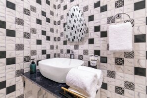 A bathroom with a white sink, black and white patterned tiles, a towel rack, and a towel. - Alaya Stays Krishna Farm With Pool (Noida)