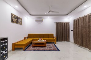 A living room with a sofa, coffee table, and a speaker. - Alaya Stays Krishna Farm With Pool (Noida)
