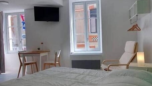 A bedroom with a large bed, a desk, and a chair. There is a TV mounted on the wall and a window with curtains. - Pleasant studio Bourgueil center (Bourgueil)