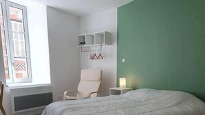 A bedroom with a large bed, a chair, a nightstand, and a green accent wall. - Pleasant studio Bourgueil center (Bourgueil)