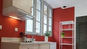 Eine kleine Küche mit roter Wand, weißem Schrank, Fenster und Holzstuhl.