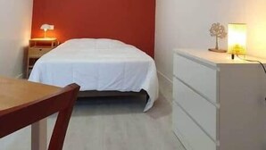 Ein Hotelzimmer mit einem Bett, einem Schreibtisch, einem Sessel, einer Kommode und einem an der Wand befestigten Fernseher.