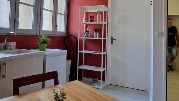 Eine kompakte Küche mit einem Holztisch, einem weißen Regal und einer roten Akzentwand.