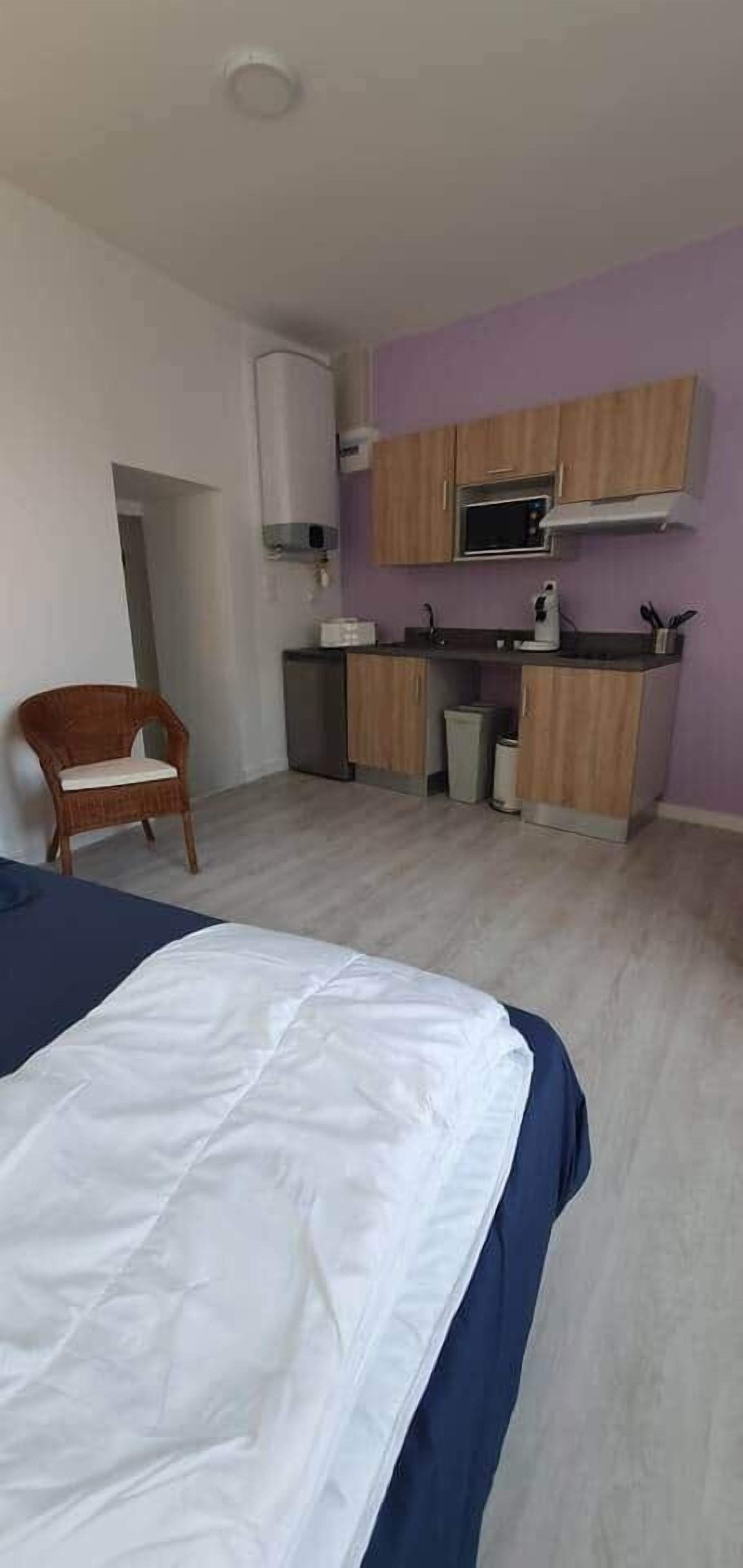 A compact room with a bed, a chair, a kitchenette, and a small bathroom.