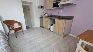 A compact kitchen with a microwave, sink, and cabinets. There is a wicker chair and a small table with a wooden top.
