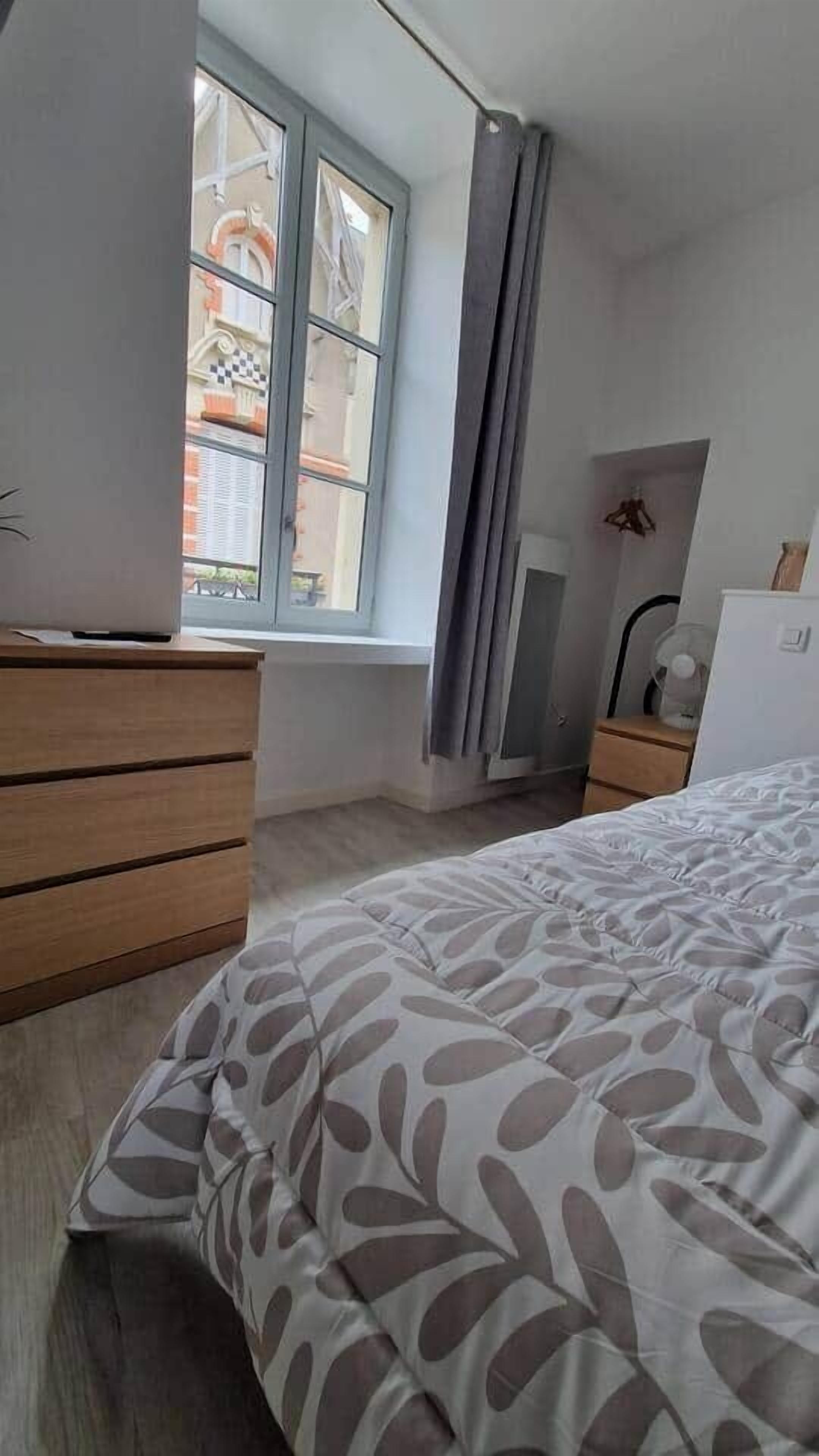 Ein Schlafzimmer mit einem Bett, einem Schminktisch, einem Fenster mit Vorhängen, einem Heizkörper und einem Ventilator.