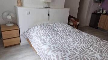 Een slaapkamer met een groot bed, een nachtkastje met een lamp, een ventilator en een kledingkast.