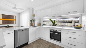 A modern kitchen with white cabinetry, a dishwasher, and a built-in oven. - 5 bedroom house, walk to beach (Alexandra Headland)