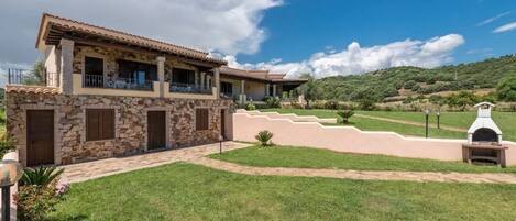 A two-story house with stone walls and a tiled roof, a paved driveway, and a grassy lawn.