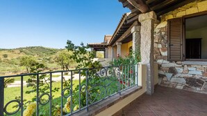Un balcon avec un mur en pierre, une rambarde en métal et une vue sur un paysage verdoyant.