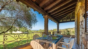 Un espace extérieur abrité, aménagé pour les repas, avec une table dressée pour quatre personnes, entouré de chaises blanches et offrant une vue sur un paysage pittoresque.
