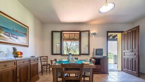 Un coin repas avec une table dressée pour quatre personnes, des meubles en bois, un panier de fruits et un tableau accroché au mur.
