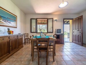 A dining area with a table set for four, wooden cabinets, a fruit bowl, and a painting on the wall. - Cozy home near the sea (Iscra E Voes)