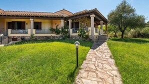 Une maison à deux étages, avec un chemin de pierre menant à l’entrée, entourée d’une végétation luxuriante.