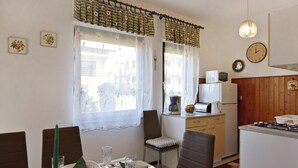 Una zona de dinar amb taula preparada per a quatre, cuina amb electrodomèstics bàsics i un rellotge a la paret.