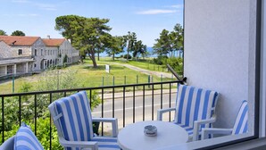 A balcony with two striped chairs and a small table, overlooking a street with buildings and trees. - Sea view apartment in Umag (Umag)