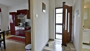 A modern kitchen with red cabinets, a microwave, and a coffee maker. There is a dining area with a table and chairs. The hallway leads to a bathroom with a sink and toilet. - Sea view apartment in Umag (Umag)