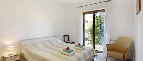 Un dormitorio con una cama, una silla, una mesita de noche y una ventana con cortinas.