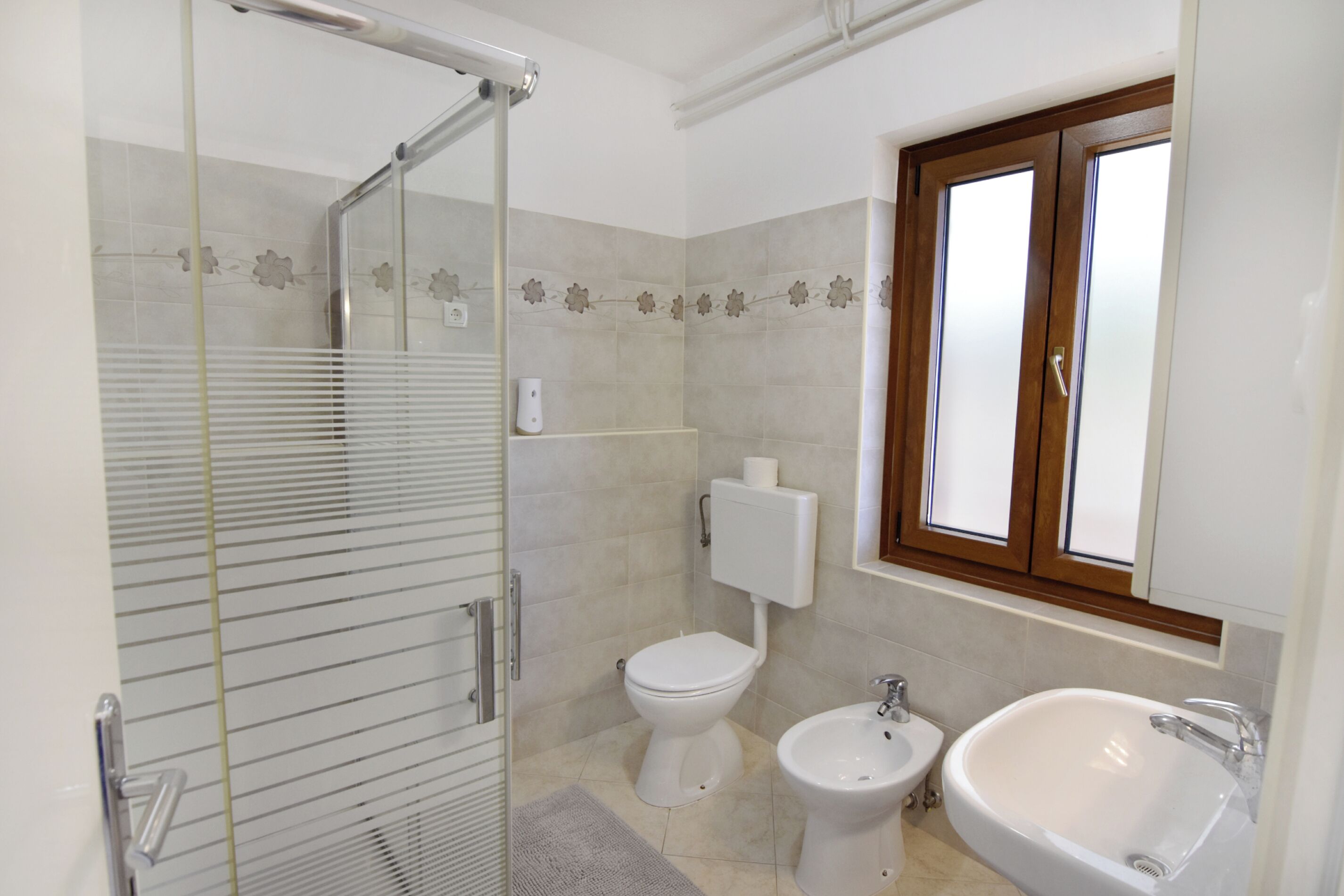 Un bany amb dutxa de vidre, vàter, bidet i rentapel.