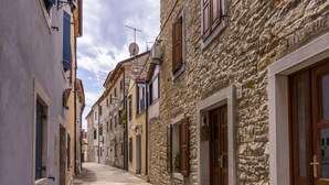 A narrow street lined with traditional stone buildings, featuring wooden doors and shutters, under a partly cloudy sky. - Terrace flat 300 mt from beach (Zambratija)