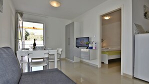 A modern living room with a grey sofa, a dining table with chairs, a TV, and a small kitchenette area. - Terrace flat 300 mt from beach (Zambratija)