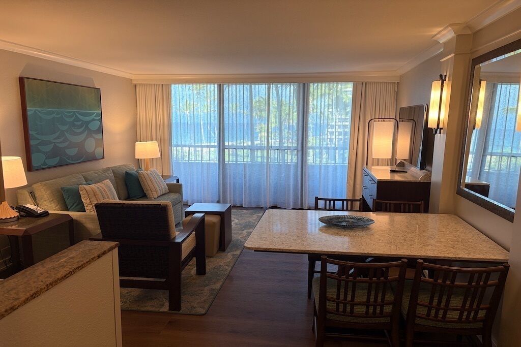 A hotel room with a living area, dining table, and a large window with curtains.