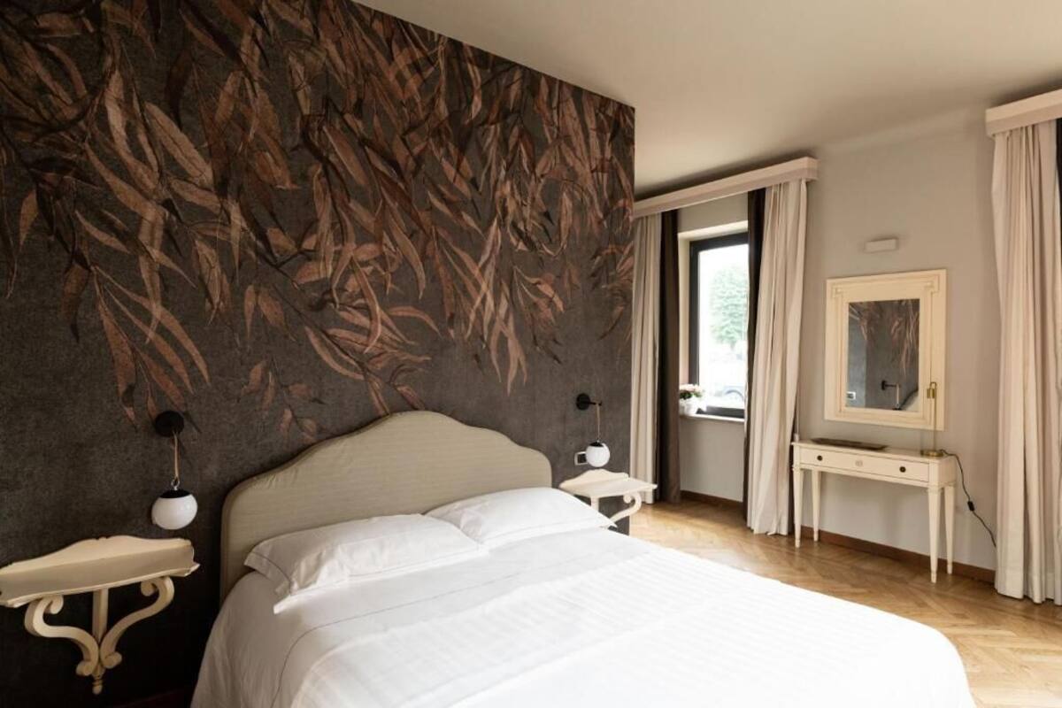 Une chambre à coucher avec un grand lit, une table de chevet, une commode, un miroir et une fenêtre avec des rideaux.