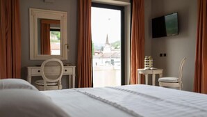 Habitación de hotel con cama, escritorio con silla, una mesita con otra silla, televisor en la pared y vista a un edificio.