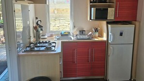 A compact kitchen with a gas stove, microwave, and refrigerator, wooden cabinets, and a window with a stone wall view. - Quiet chalet under the trees 3 km from Bonifacio and 2 km from the beaches (Bonifacio)